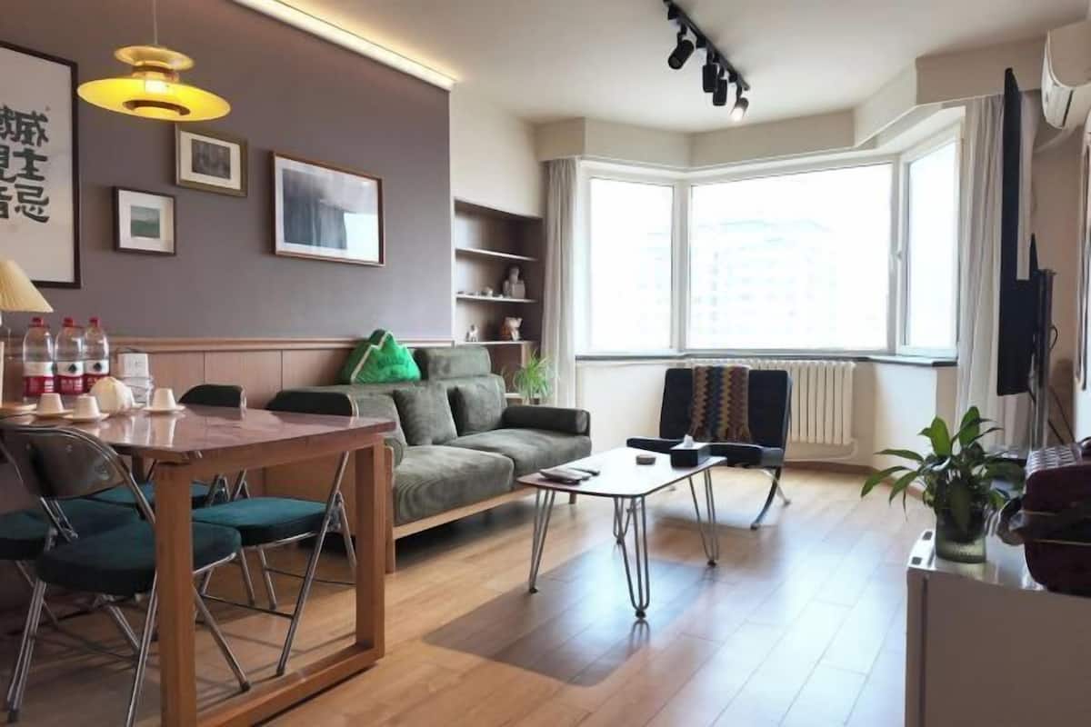 Een moderne woonkamer met een bank, salontafel en eethoek. Een groot raam zorgt voor natuurlijk licht en uitzicht op de stad.