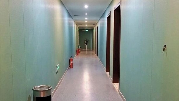 Un long couloir étroit aux murs bleu clair et au sol gris, qui mène à une porte au fond.