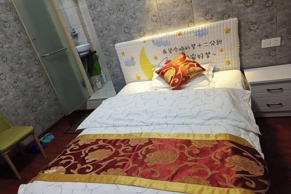 Una cama bien hecha con un cabecero decorativo, una silla verde y una mesita con mantel verde.