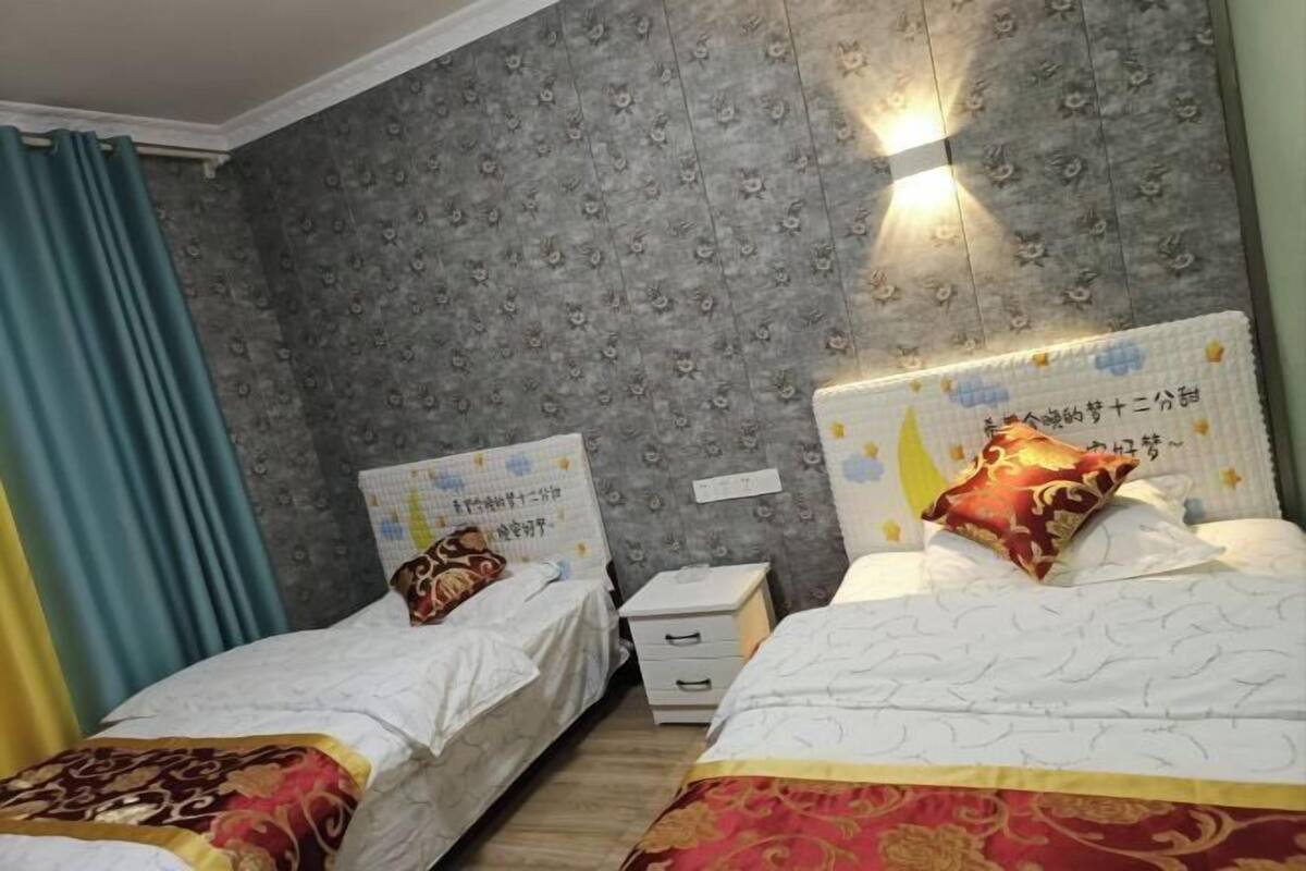 Habitación de hotel con dos camas, una mesita de noche y una pared decorada con motivos florales.