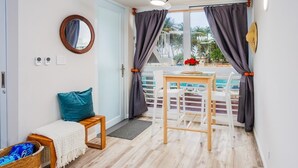 A room with a ceiling fan, a small table with chairs, a bench with a cushion, a wicker basket, and a view of a pool and palm trees outside.