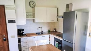 Een kleine keuken met witte kastjes, een roestvrijstalen koelkast, een houten tafel en een koffiezetapparaat.