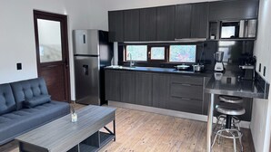 A modern kitchen with dark wood cabinets, a stainless steel refrigerator, and a built-in oven. There's a wooden bench and a stool near the kitchen.