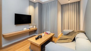 A modern living room with a flat-screen TV, wooden coffee table, sofa, and a large window with curtains. - Morich Suite Antasari (Jakarta)