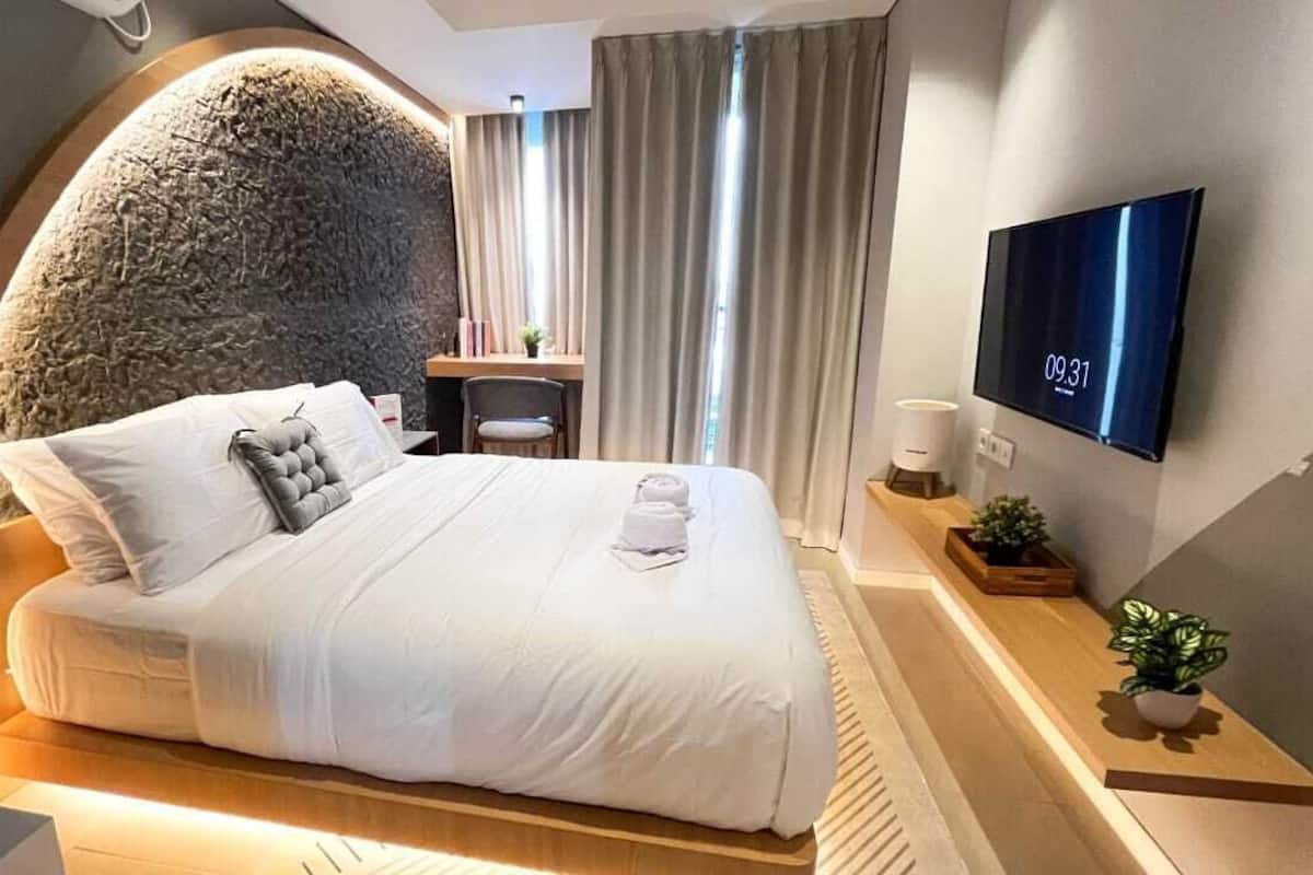 A modern hotel room with a large bed, a TV mounted on the wall, and a desk with a chair.