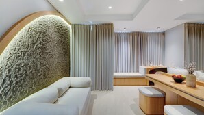A modern hotel room with a stone accent wall, a sofa, a wooden desk, and a dining area. - Morich Suite Antasari (Jakarta)