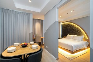 A modern hotel room with a dining area, a bed with a unique stone wall, and a small desk. - Morich Suite Antasari (Jakarta)
