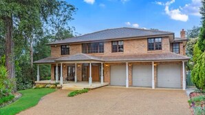 Une maison à deux étages, avec une façade en briques, un porche couvert et une allée menant à un garage.