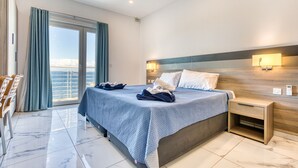 Habitación de hotel moderna con una cama grande, dos mesitas de noche, vista al mar y un balcón.