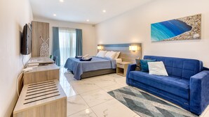 A modern hotel room with a bed, a blue sofa, a desk with a flat-screen TV, and a large abstract painting on the wall. - Stylish Apartment in Bay Square 1 (St. Paul's Bay)