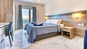 A modern hotel room with a bed, bedside table, and a view of the sea. - Stylish Apartment in Bay Square 1 (St. Paul's Bay)