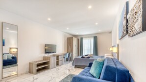 Quarto de hotel moderno com uma cama grande, um sofá azul, uma televisão e uma escrivaninha.