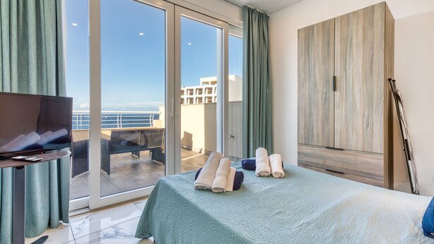 Habitación de hotel con cama, televisor, balcón y vistas al mar, además de un amplio armario de madera.