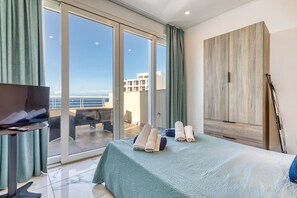 Une chambre d’hôtel avec un lit, une télévision, un balcon donnant sur la mer et une grande armoire en bois.