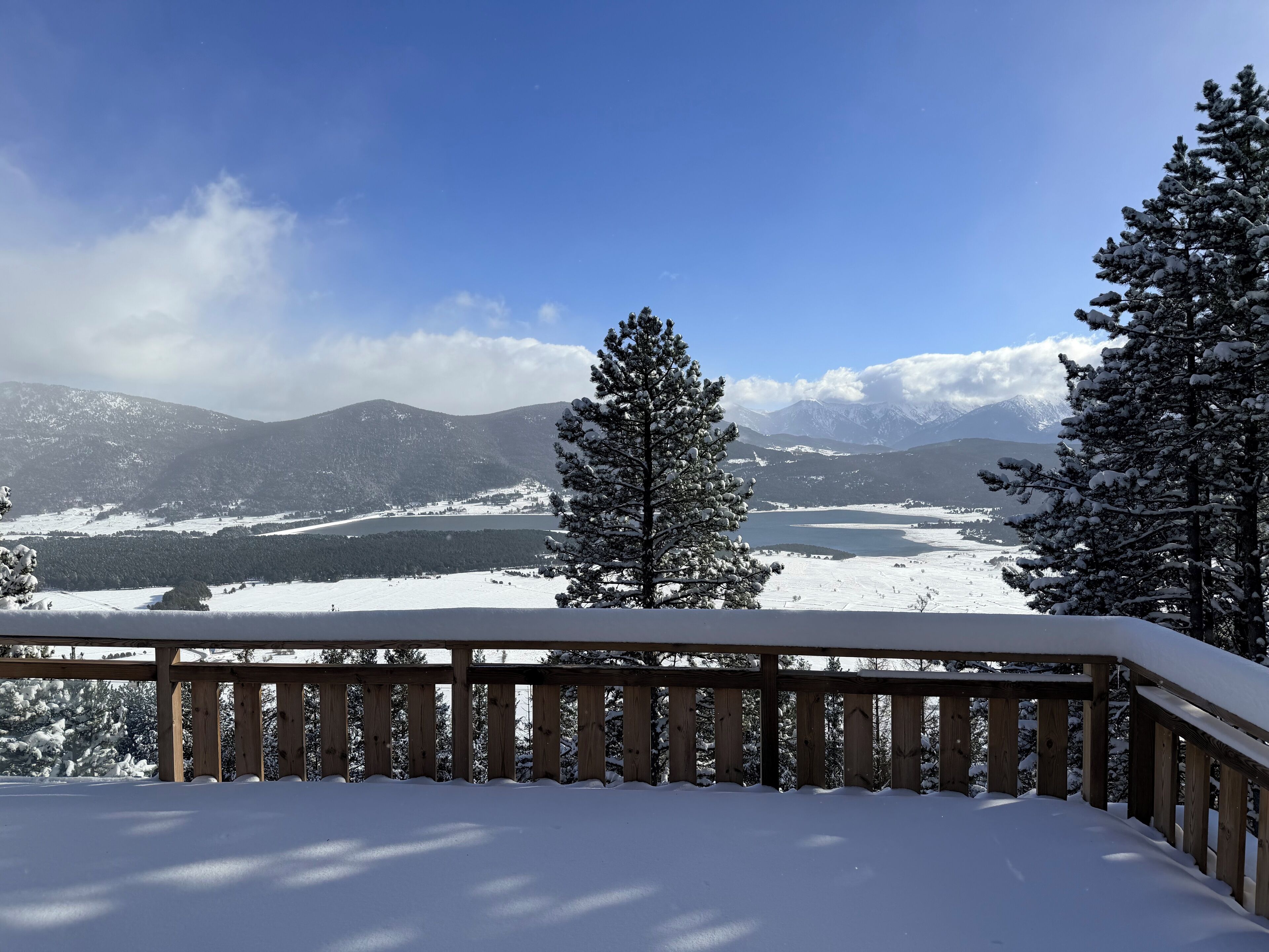 A snow-covered deck with a view of a lake and mountains.