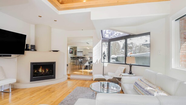 A modern living room with a fireplace, white furniture, and a large window offering a view of the outdoors. - Pet-Friendly Penthouse with Shared Hot Tub (Telluride)