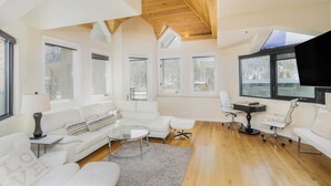 A modern living room with a white sofa, a glass coffee table, and a wooden ceiling. - Pet-Friendly Penthouse with Shared Hot Tub (Telluride)
