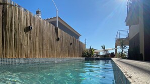 A swimming pool with clear water, a bamboo fence, and a building with a balcony in the background. - Quiet Algarve villa near Albufeira & branches with prívate pool BBQ terrace (Algoz)