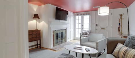 A living room with a fireplace, a television mounted on the wall, a sofa, a coffee table, and a lamp.