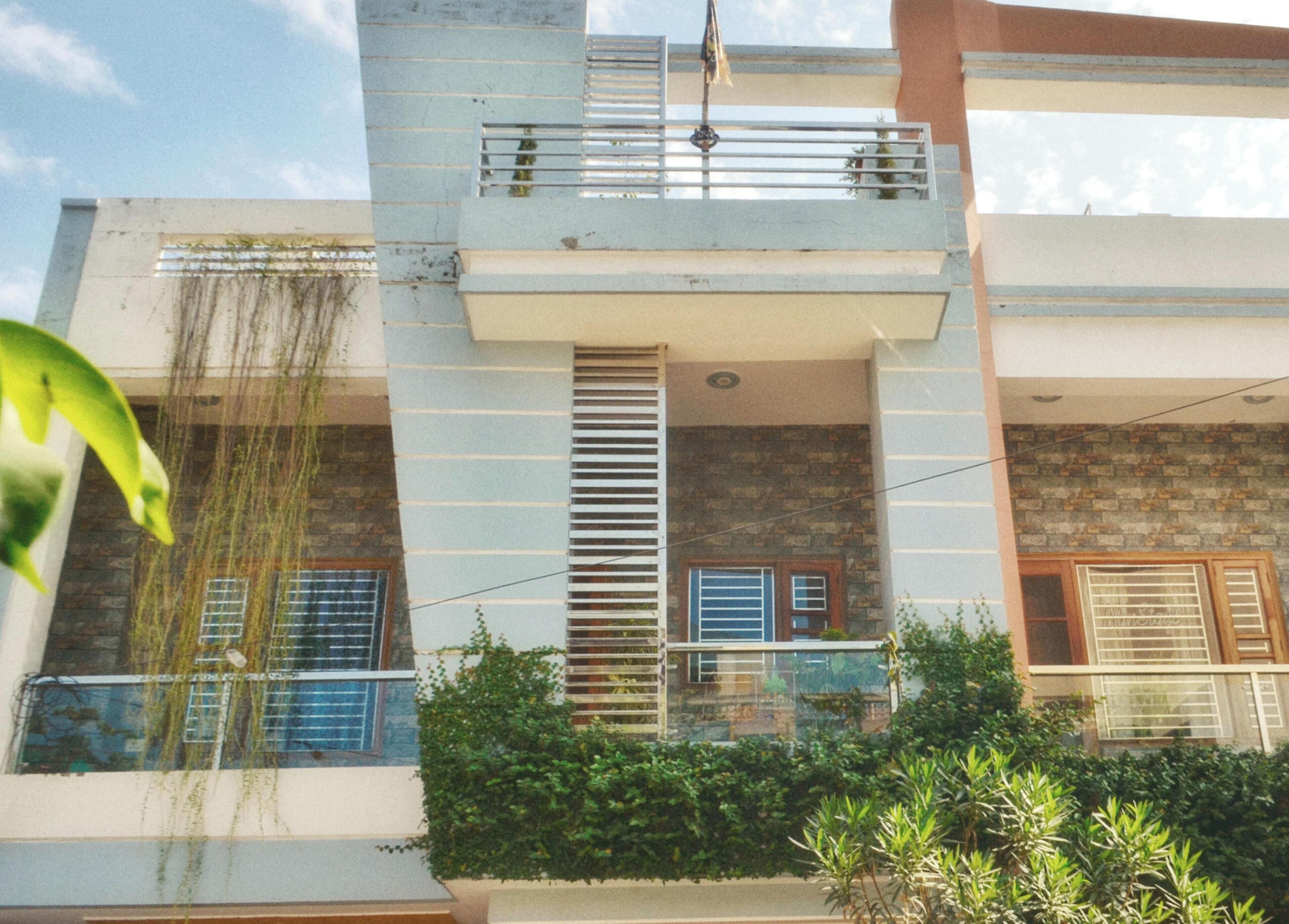 A multi-story building with a balcony, a window with a shutter, and a door.