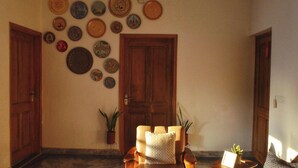 A room with a wooden door, a wall decorated with various plates, a chair with a cushion, and a small table with a plant. - 15 minutes to the Harkipauri! Manstays 3 bedroom condo with Balcony & parking! (Haridwar)