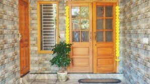 A wooden door with a window, a potted plant, and a stone wall. - 15 minutes to the Harkipauri! Manstays 3 bedroom condo with Balcony & parking! (Haridwar)