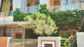 A building with a stone facade, multiple windows with wooden shutters, and a balcony with a metal railing. - 15 minutes to the Harkipauri! Manstays 3 bedroom condo with Balcony & parking! (Haridwar)