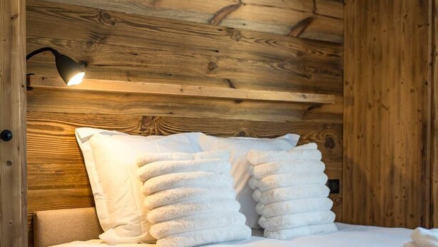 A neatly made bed with white linens and pillows, a wooden headboard, and a wall-mounted lamp. - Apartment for 8 people in a new residence on the slopes (LA TOUSSUIRE)