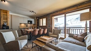 A modern living room with a sofa, chairs, a coffee table, and a dining area with a table and chairs. There is a large window with a view of a snowy landscape. - Apartment for 8 people in a new residence on the slopes (LA TOUSSUIRE)