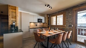 A modern kitchen with a central island, a dining area with six chairs, and a stone accent wall. - Apartment for 8 people in a new residence on the slopes (LA TOUSSUIRE)