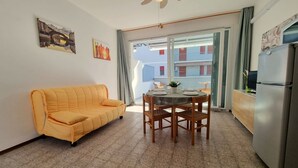 Un espace de vie compact comprenant un canapé, une table à manger, des chaises, un ventilateur de plafond et un réfrigérateur.