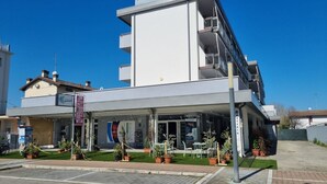 Un bâtiment moderne doté d’un toit plat, d’un balcon à l’étage supérieur et d’un espace d’entrée abrité agrémenté de plantes en pot.