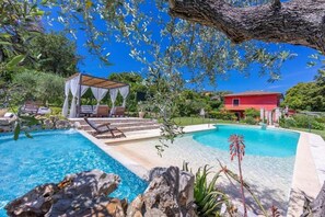 Una piscina con un pabellón, una casa roja y abundante vegetación.