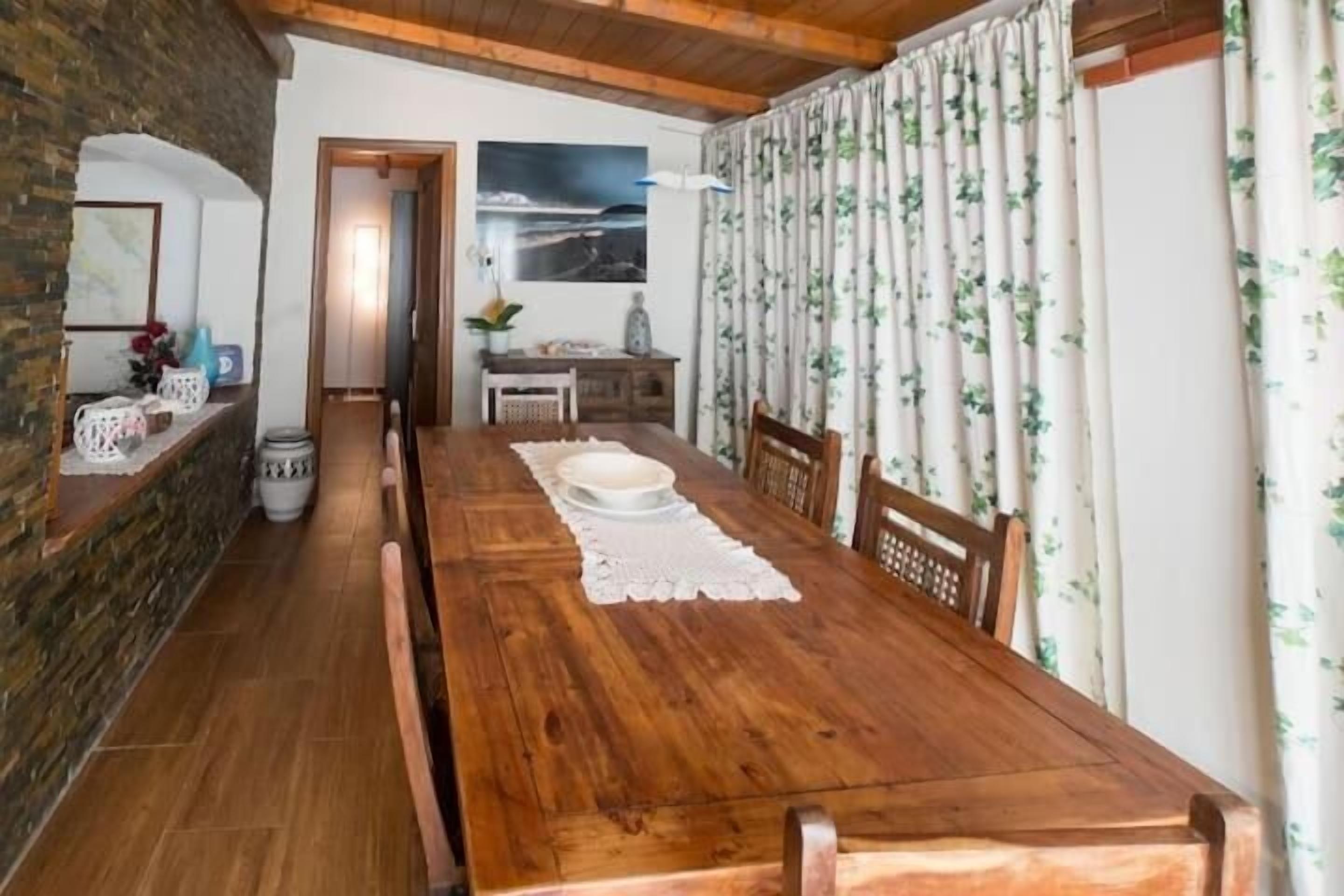 A dining area with a wooden table, chairs, and a view of the sea through a window.