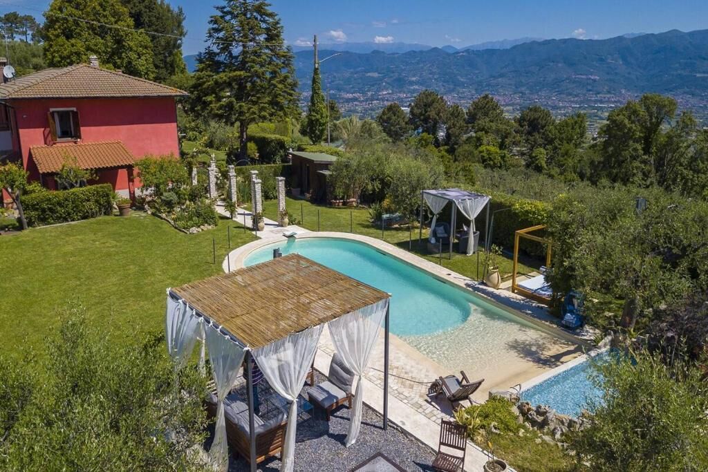 Une piscine privée agrémentée d’un belvédère et de meubles de jardin, le tout entouré d’une végétation luxuriante et offrant une vue sur les montagnes lointaines.