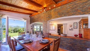 A dining area with a wooden table set for six, a stone wall, and a view of the outdoors. - la casa fra gli ulivi (Montemarcello)