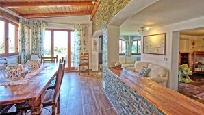 A dining area with a wooden table and chairs, a stone accent wall, and a sofa in the background. - la casa fra gli ulivi (Montemarcello)