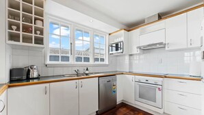 Una cocina moderna con armarios blancos, encimera de madera, lavavajillas, horno y ventana con vistas al tejado.