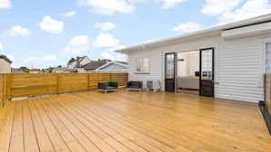 Una terraza de madera con dos sillas y una mesa, una casa blanca con puerta corredera y una valla de madera.