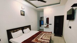 A bedroom with a bed, a ceiling fan, a TV, and a mirror. - Hotel Hare Krishna Vrindavan (Vrindavan)