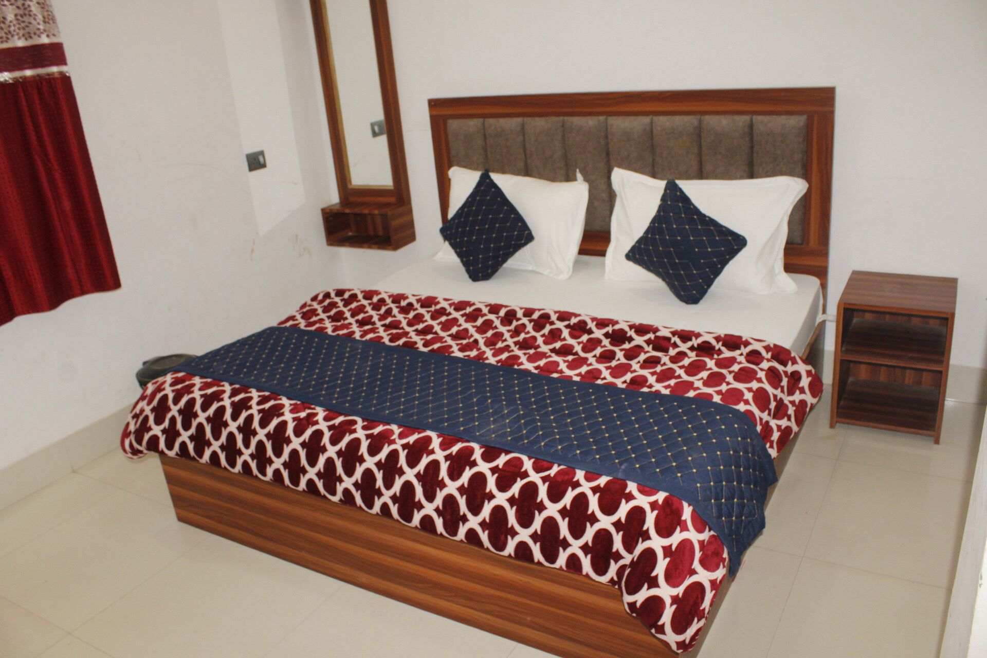 Un dormitorio con cabecera de cama de madera, colcha estampada, dos almohadas y una mesita de noche.