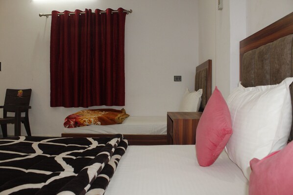A bedroom with a bed, a nightstand, a chair, and a red curtain. - Hotel Hare Krishna Vrindavan (Vrindavan)