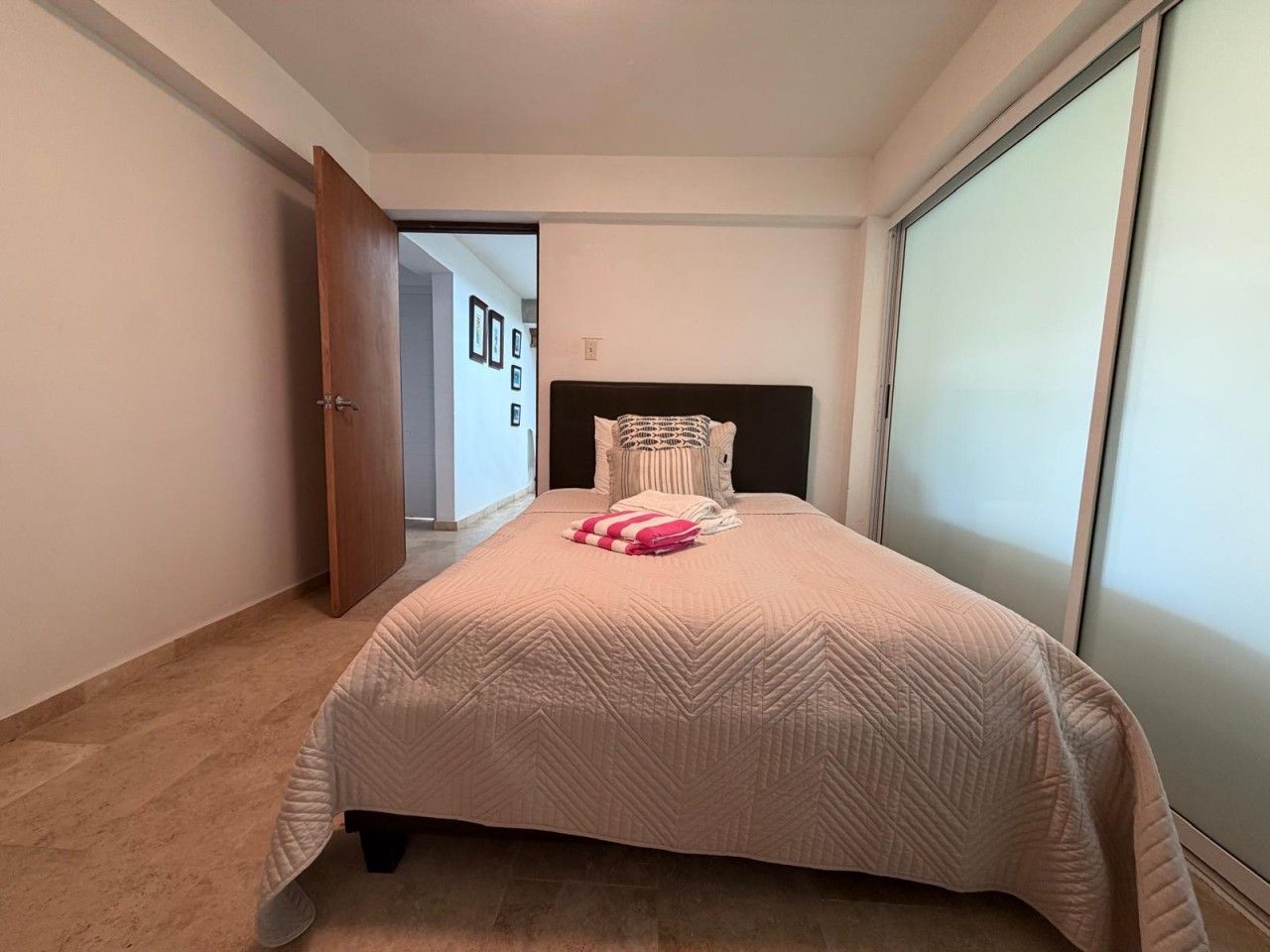 A bedroom with a bed, a door, a wall, and a window.