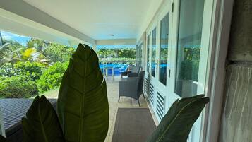A covered outdoor area with large green leaves, a patio with a chair, and a view of the outdoors.