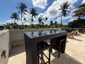 An outdoor seating area with a glass-top table and chairs, surrounded by palm trees and a clear sky. - Villa Capitan | Spacious House W/ Pool & Beach (Vega Alta)
