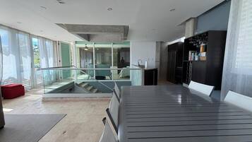 A modern interior with a glass railing, a red bench, and a kitchen area.