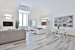 Un salon moderne comprenant un canapé, une table à manger avec des chaises, un téléviseur fixé au mur et une grande fenêtre.