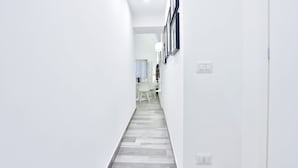 Un pasillo con paredes blancas, un suelo estampado y una zona de comedor con sillas y una mesa a lo lejos.
