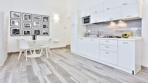 Una cocina moderna con armarios blancos, un microondas integrado y un comedor con mesa y sillas blancas.