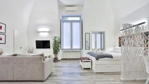 Una sala de estar moderna con sofá, cama, televisor y un ventanal grande.